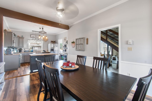 dining room with crown molding, beamed ceiling, ceiling fan with notable chandelier, and dark hardwood / wood-style floors