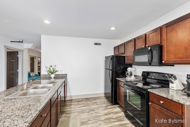 kitchen featuring light stone countertops, black appliances, sink, and light wood-type flooring