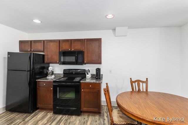 kitchen with stone countertops, black appliances, and wood-type flooring