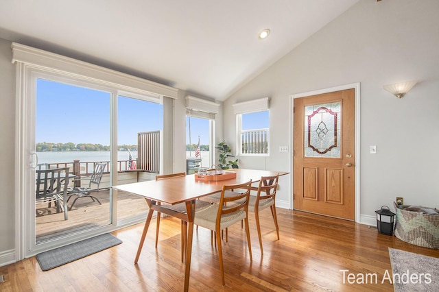 dining space featuring hardwood / wood-style flooring, high vaulted ceiling, a water view, and a wealth of natural light