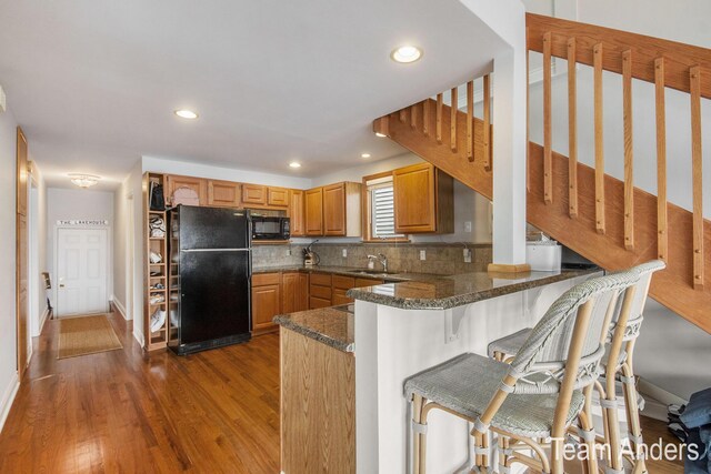 kitchen with dark wood-type flooring, backsplash, kitchen peninsula, a breakfast bar, and black appliances