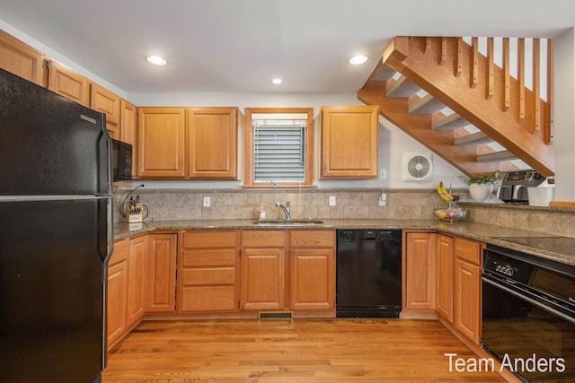 kitchen with stone counters, black appliances, sink, light hardwood / wood-style flooring, and tasteful backsplash