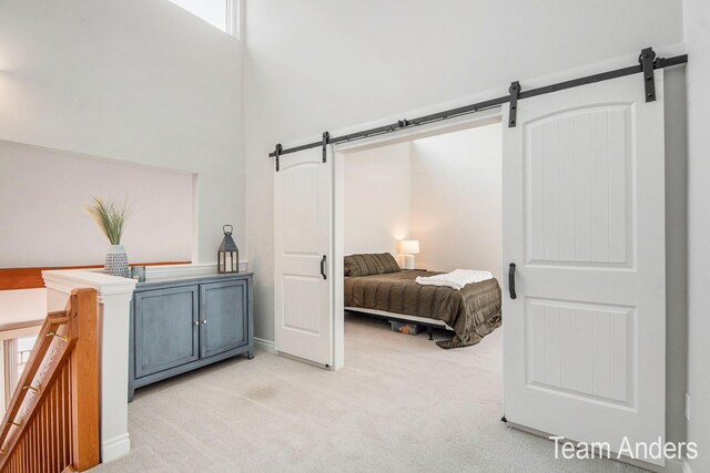 bedroom with multiple windows, light carpet, a towering ceiling, and a barn door