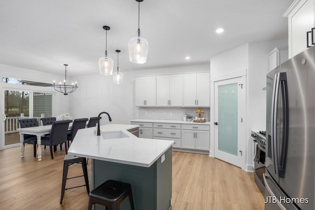 kitchen with a center island with sink, sink, hanging light fixtures, white cabinetry, and stainless steel appliances