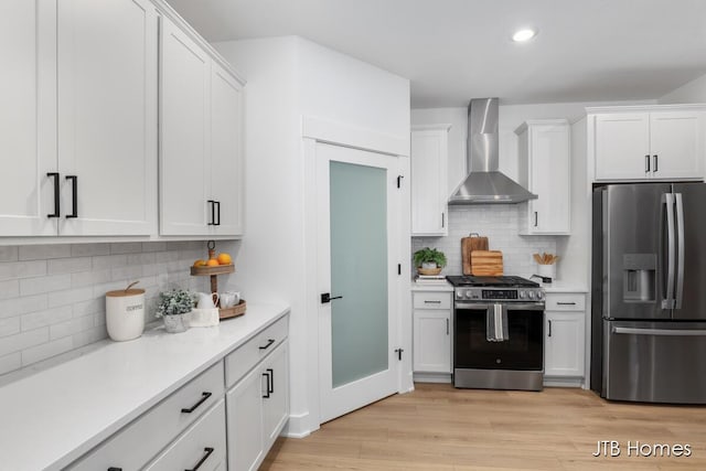 kitchen featuring wall chimney exhaust hood, white cabinetry, stainless steel appliances, and light hardwood / wood-style flooring