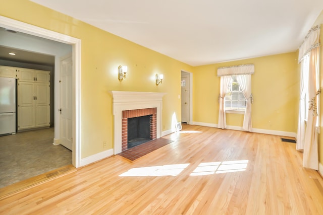 unfurnished living room with light hardwood / wood-style flooring and a brick fireplace