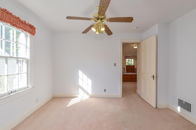 empty room featuring ceiling fan, a healthy amount of sunlight, and light colored carpet