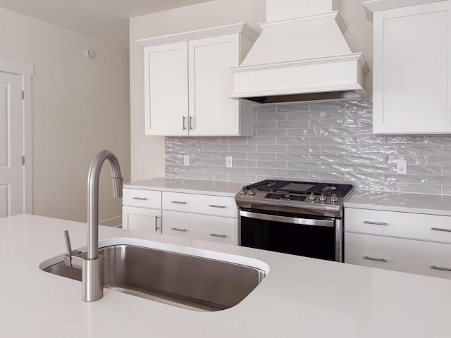 kitchen featuring stainless steel range, premium range hood, white cabinets, and sink