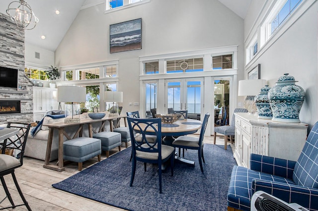 dining room featuring light hardwood / wood-style flooring, a fireplace, high vaulted ceiling, and a healthy amount of sunlight