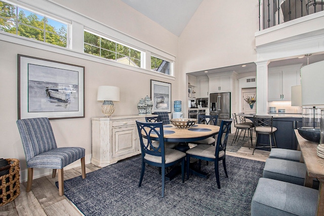 dining area featuring wood-type flooring, decorative columns, and high vaulted ceiling