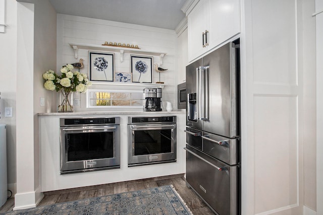 kitchen with appliances with stainless steel finishes, dark hardwood / wood-style flooring, and white cabinets