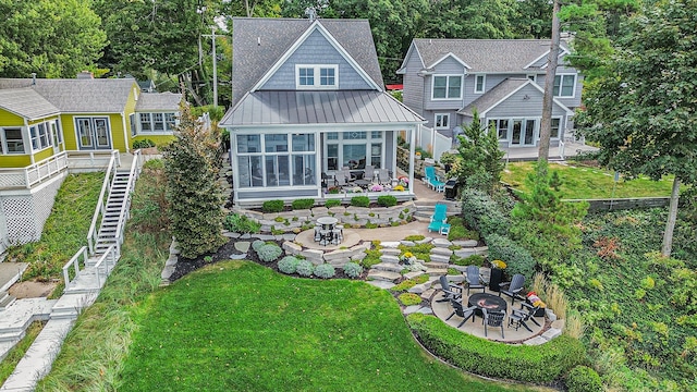 rear view of property with a sunroom, a yard, a patio area, and a fire pit