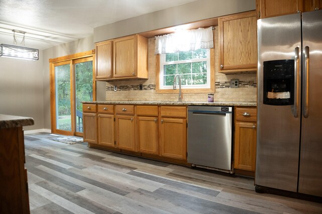 kitchen with stainless steel appliances, backsplash, light wood-type flooring, and a healthy amount of sunlight