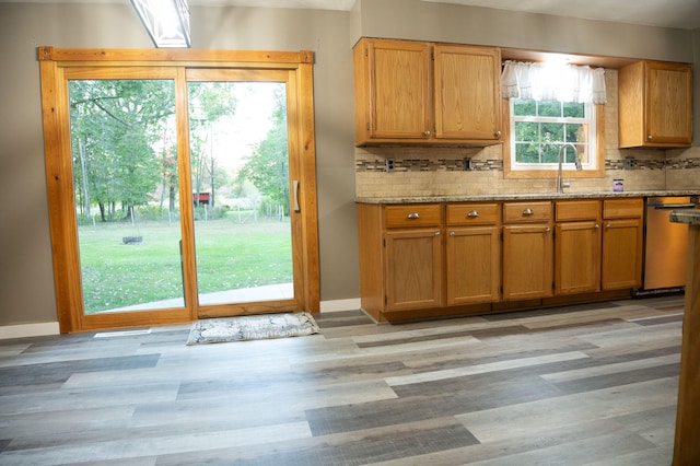 kitchen with light wood-type flooring, a healthy amount of sunlight, stainless steel dishwasher, and backsplash