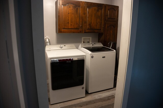 washroom with light wood-type flooring, washing machine and clothes dryer, and cabinets