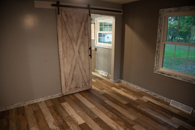 spare room with a barn door, hardwood / wood-style floors, and a healthy amount of sunlight