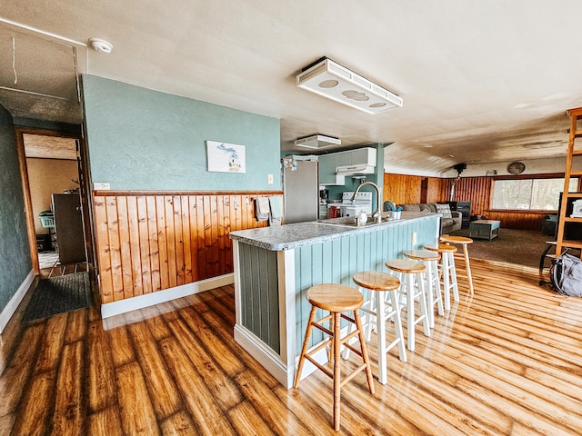 kitchen featuring stainless steel refrigerator, wood-type flooring, a breakfast bar area, wooden walls, and kitchen peninsula