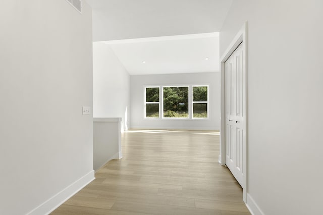 hallway with light wood-type flooring and lofted ceiling