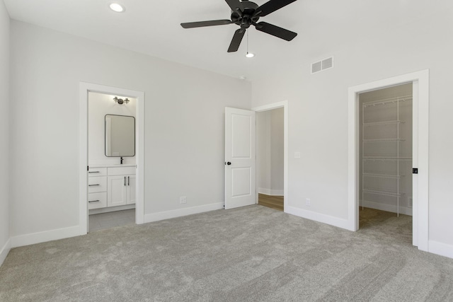 unfurnished bedroom with light colored carpet, a walk in closet, ensuite bathroom, and ceiling fan