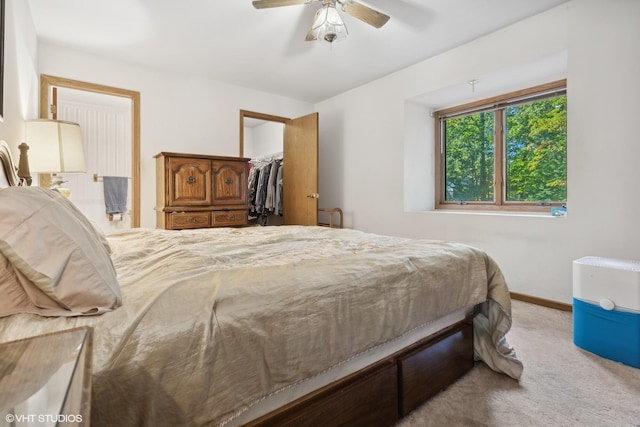 bedroom featuring a walk in closet, light colored carpet, a closet, and ceiling fan