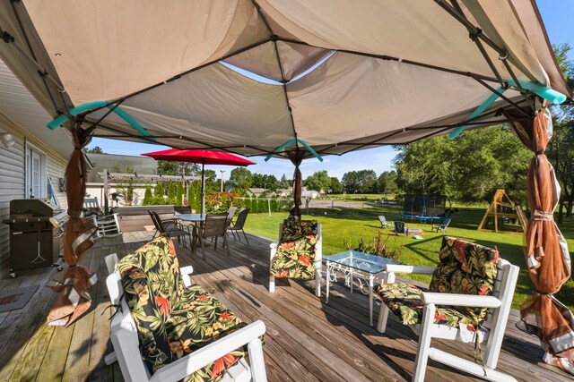 wooden terrace with grilling area, a trampoline, and a lawn