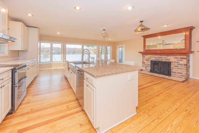 kitchen with an island with sink, stainless steel appliances, sink, light wood-type flooring, and white cabinets