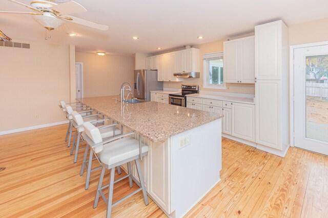 kitchen featuring appliances with stainless steel finishes, white cabinets, light wood-type flooring, and a breakfast bar area