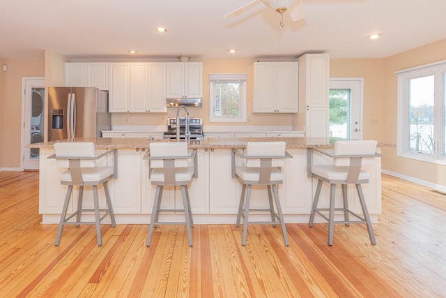 kitchen featuring light hardwood / wood-style floors, stainless steel appliances, white cabinets, a breakfast bar area, and a kitchen island with sink