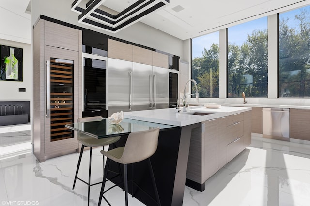 kitchen with sink, beverage cooler, a center island with sink, dishwasher, and a kitchen bar