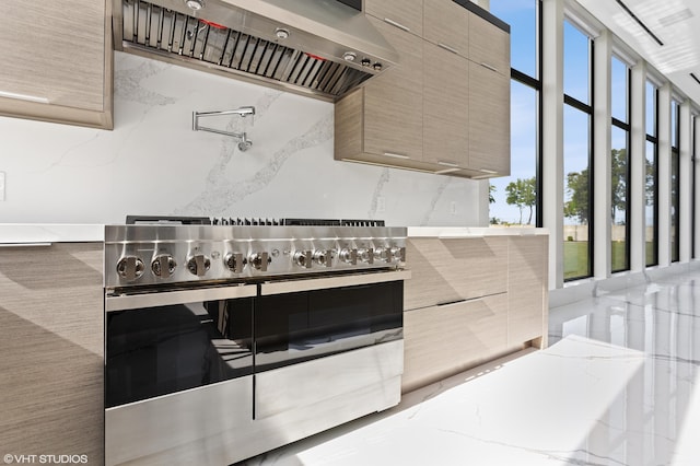 kitchen with wall chimney exhaust hood, high end stainless steel range, decorative backsplash, and light stone countertops