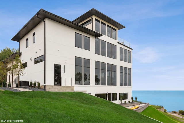 back of house with a water view, cooling unit, and a lawn