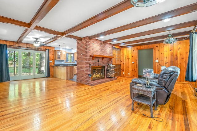 living room with beamed ceiling, light wood-type flooring, ceiling fan, wooden walls, and a fireplace