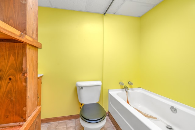 bathroom with a tub to relax in, a drop ceiling, toilet, and tile patterned floors