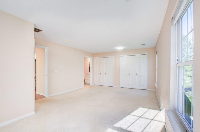 unfurnished bedroom with light carpet and multiple closets