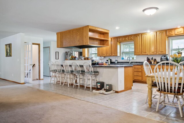 kitchen with kitchen peninsula, light colored carpet, sink, and a kitchen breakfast bar