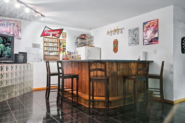 bar with rail lighting, dark tile patterned floors, and white fridge