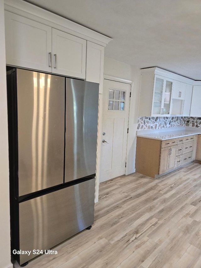 kitchen with stainless steel refrigerator, white cabinetry, light hardwood / wood-style floors, and tasteful backsplash