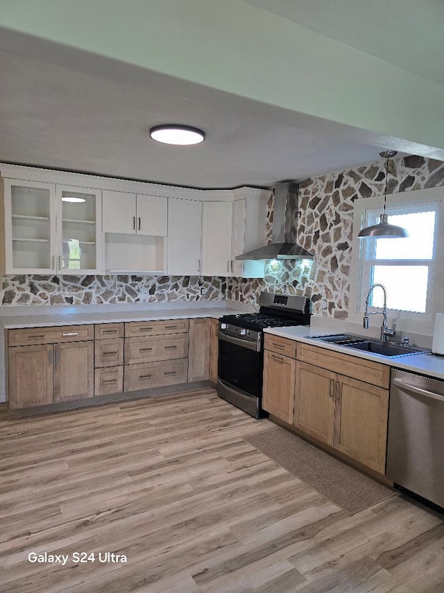 kitchen featuring sink, decorative light fixtures, wall chimney range hood, stainless steel appliances, and light wood-type flooring