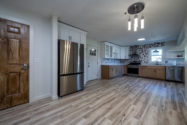 kitchen with decorative light fixtures, wall chimney exhaust hood, light hardwood / wood-style flooring, white cabinetry, and appliances with stainless steel finishes