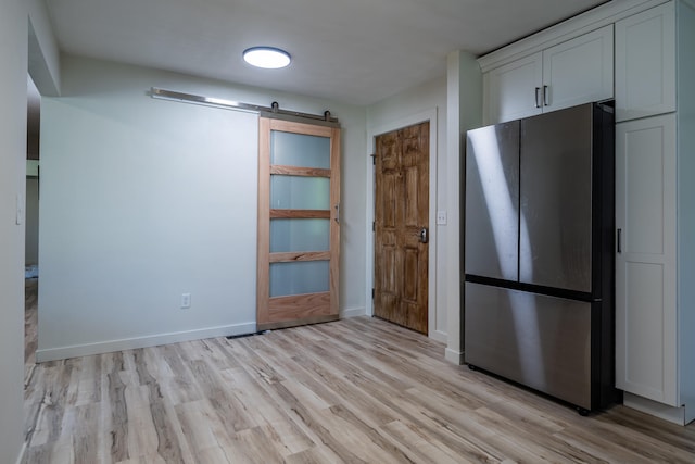 kitchen featuring a barn door, stainless steel refrigerator, white cabinetry, and light hardwood / wood-style flooring