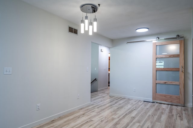 unfurnished room with a barn door and light hardwood / wood-style flooring