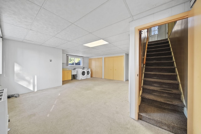 basement featuring a drop ceiling, washer and clothes dryer, and light colored carpet