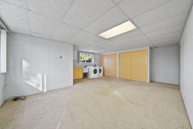 basement with a drop ceiling, light colored carpet, sink, and washer / dryer