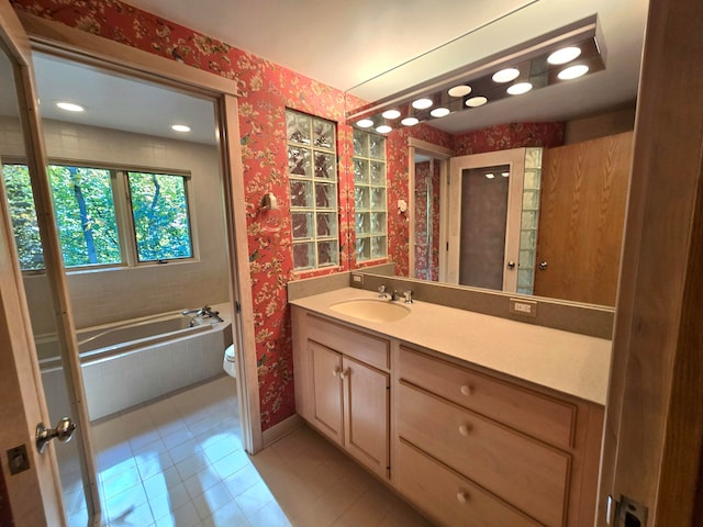 bathroom with tile patterned flooring, vanity, toilet, and tiled tub