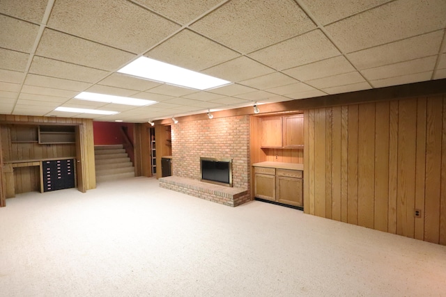 basement featuring wooden walls, light carpet, track lighting, and a brick fireplace