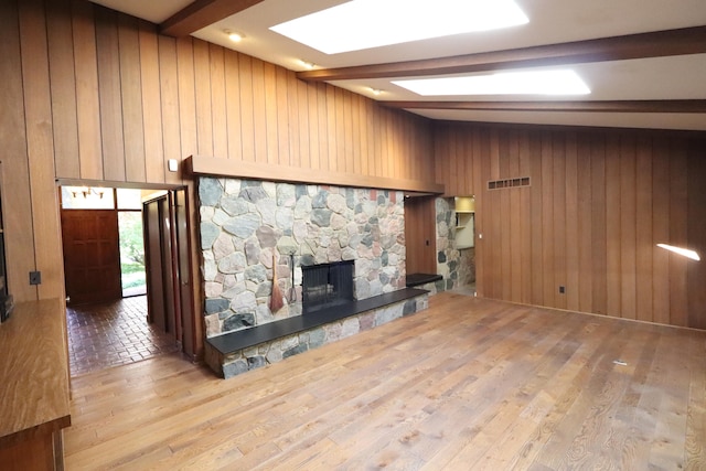 unfurnished living room with lofted ceiling with beams, light hardwood / wood-style floors, a stone fireplace, and wood walls