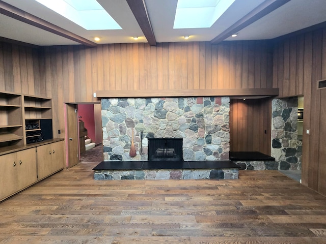 living room with beam ceiling, a stone fireplace, wood walls, and wood-type flooring