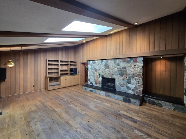 unfurnished living room featuring beam ceiling, hardwood / wood-style floors, a textured ceiling, wooden walls, and a fireplace