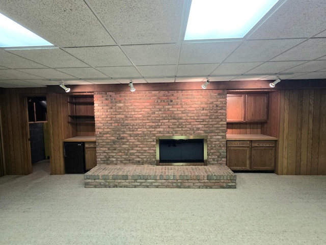 basement featuring carpet floors, wood walls, rail lighting, and a brick fireplace