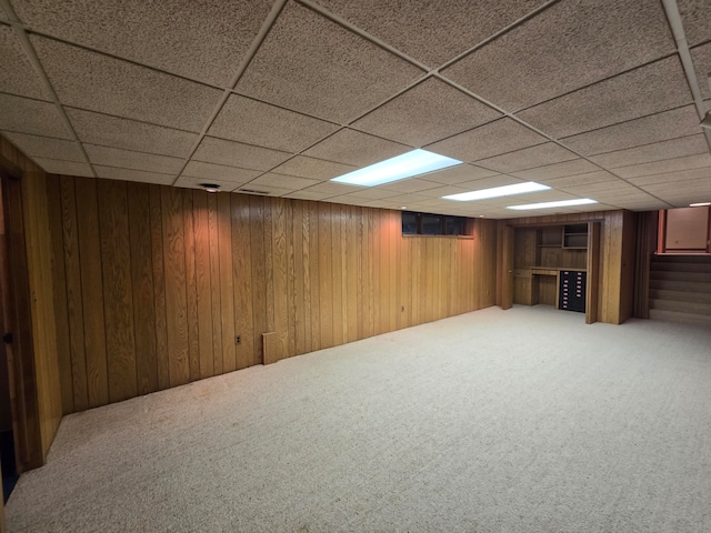 basement with carpet flooring, a paneled ceiling, and wooden walls